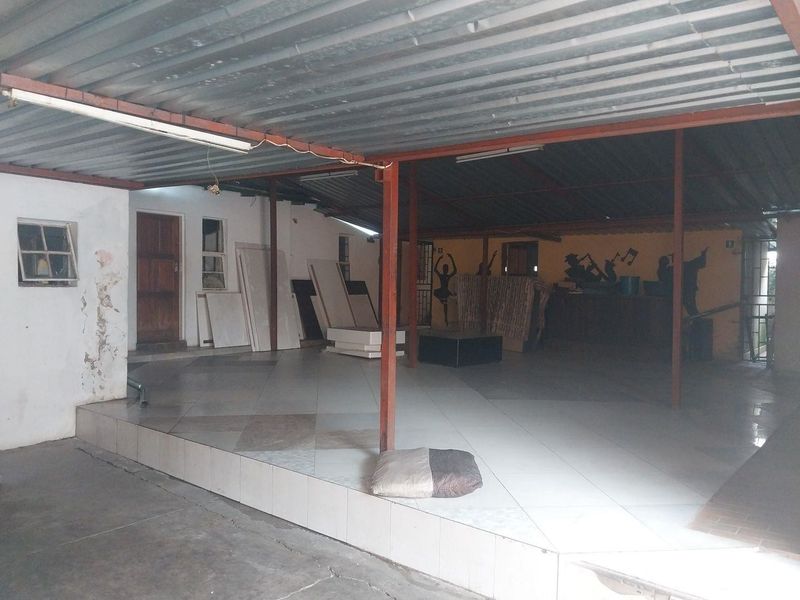 A large, covered outdoor patio area featuring a raised tiled platform, steel support columns, and a corrugated metal roof, suitable for an entertainment space.