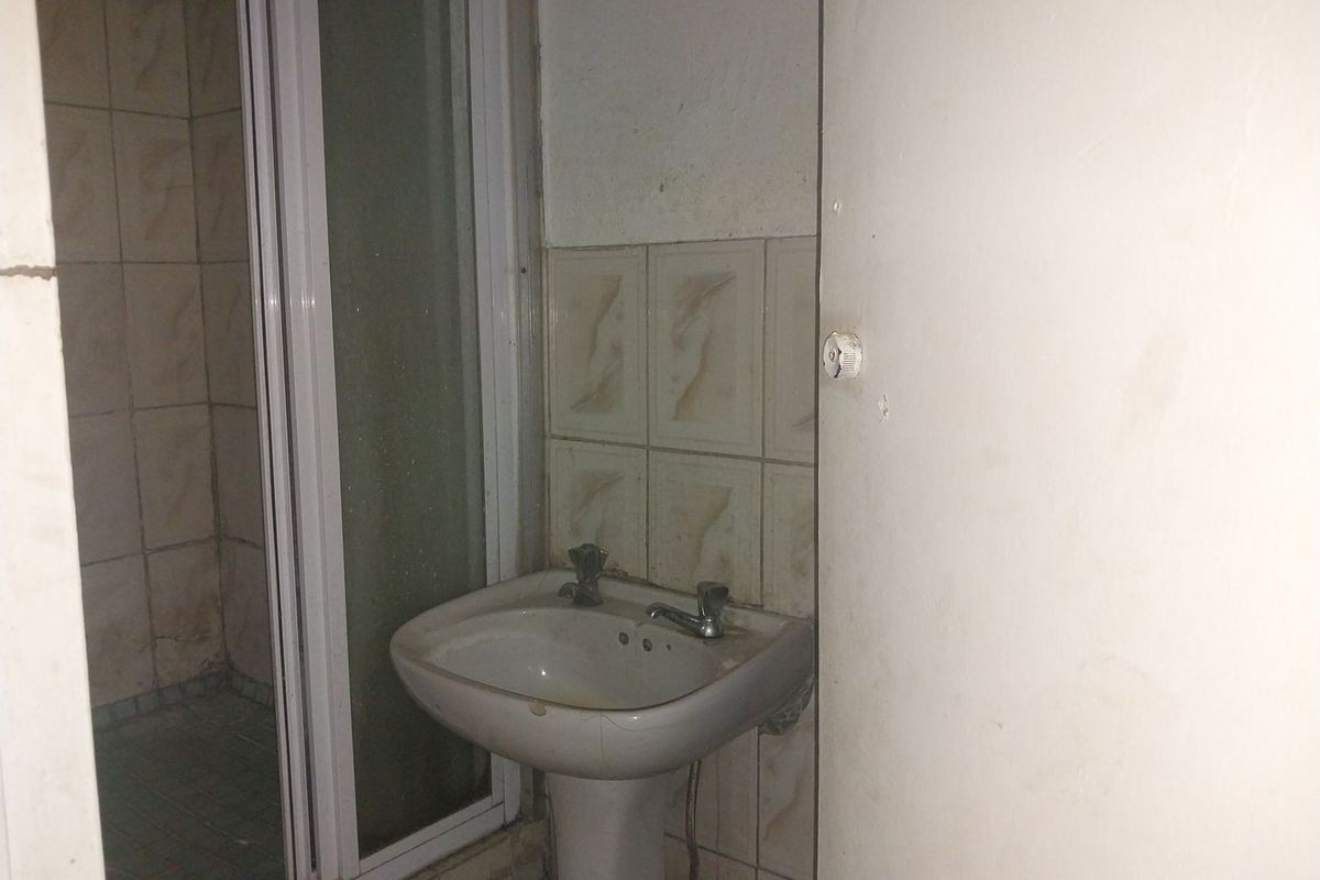 A dated bathroom featuring a pedestal basin and a shower enclosure with tiled finishes, requiring cosmetic updates and maintenance.