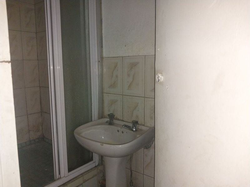A dated bathroom featuring a pedestal basin and a shower enclosure with tiled finishes, requiring cosmetic updates and maintenance.
