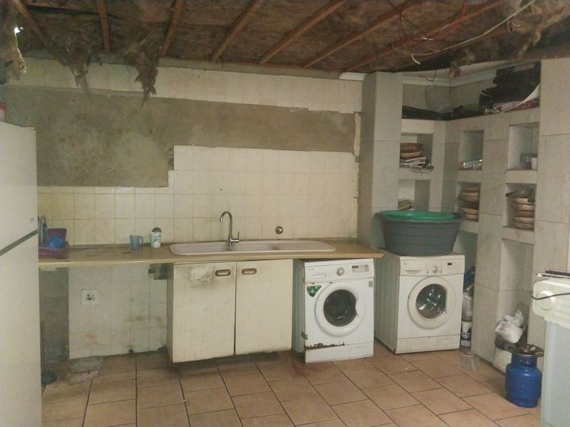 A utility laundry area featuring a built-in sink, tiled flooring, and integrated shelving, currently requiring significant renovation and finishing of walls and ceiling.