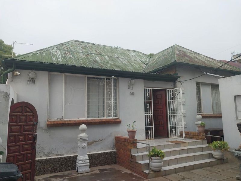 Front elevation of a single-story house featuring a corrugated metal roof, brick-stepped entrance, and security-fitted windows and doors.