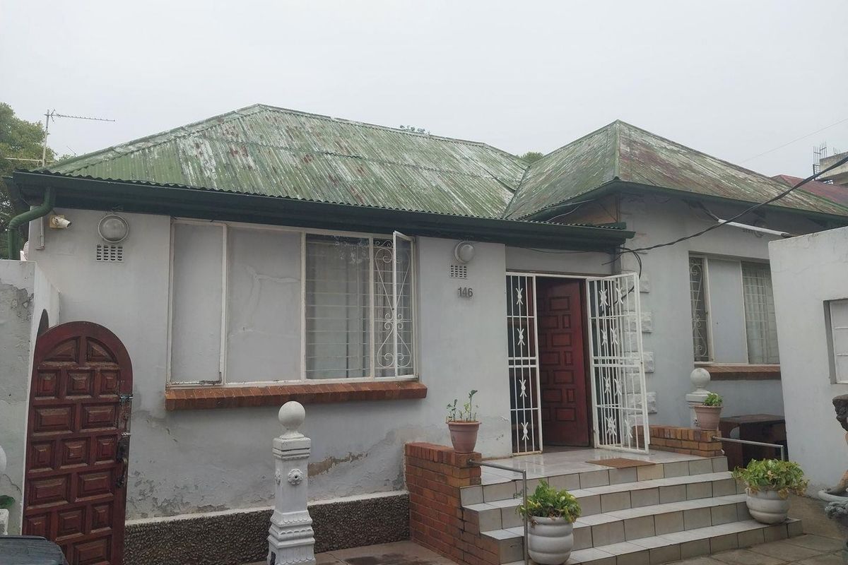 Front elevation of a single-story house featuring a corrugated metal roof, brick-stepped entrance, and security-fitted windows and doors.