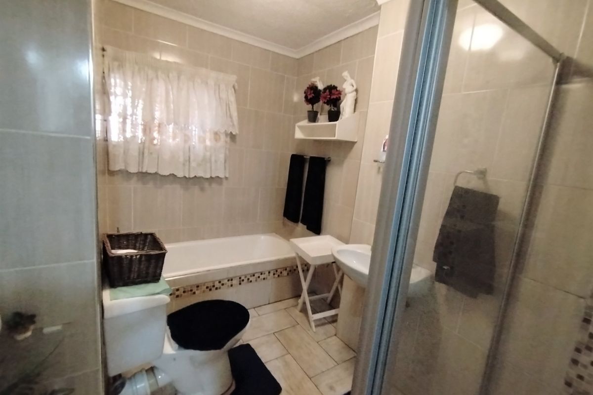 A functional bathroom featuring a bathtub, separate shower enclosure, pedestal basin, and toilet with neutral wall and floor tiling.