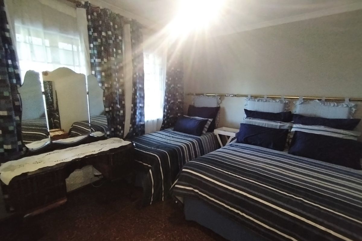 A bedroom featuring tiled flooring and coving, currently furnished with two beds and a vanity area.