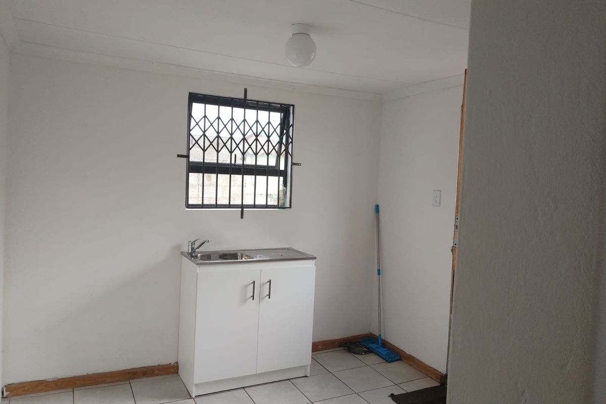 A compact kitchen area featuring a single stainless steel sink unit, tiled flooring, and a window fitted with a security gate.