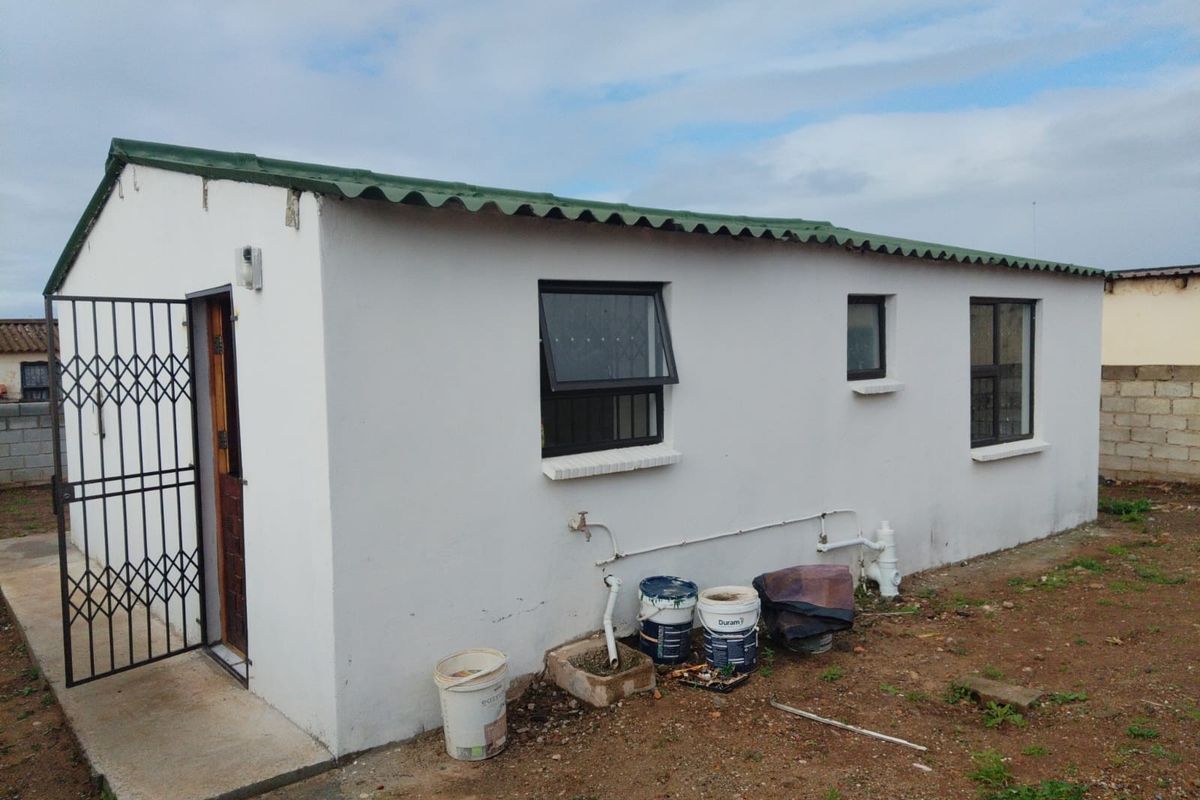 Rear view of a simple detached structure featuring a corrugated metal roof, security gate, and basic aluminium windows with exposed exterior plumbing.