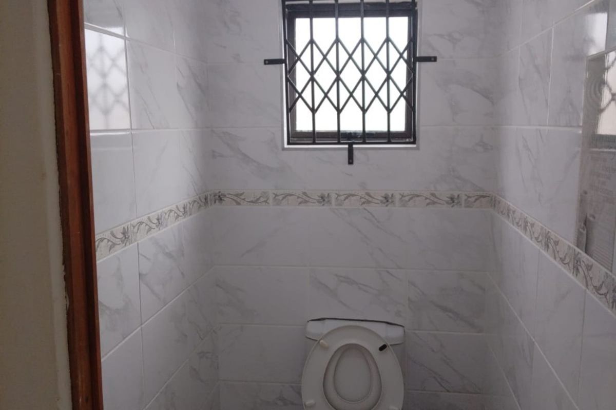 A compact, well-maintained guest bathroom featuring floor-to-ceiling marble-look wall tiles, a pedestal basin, and a secure window.