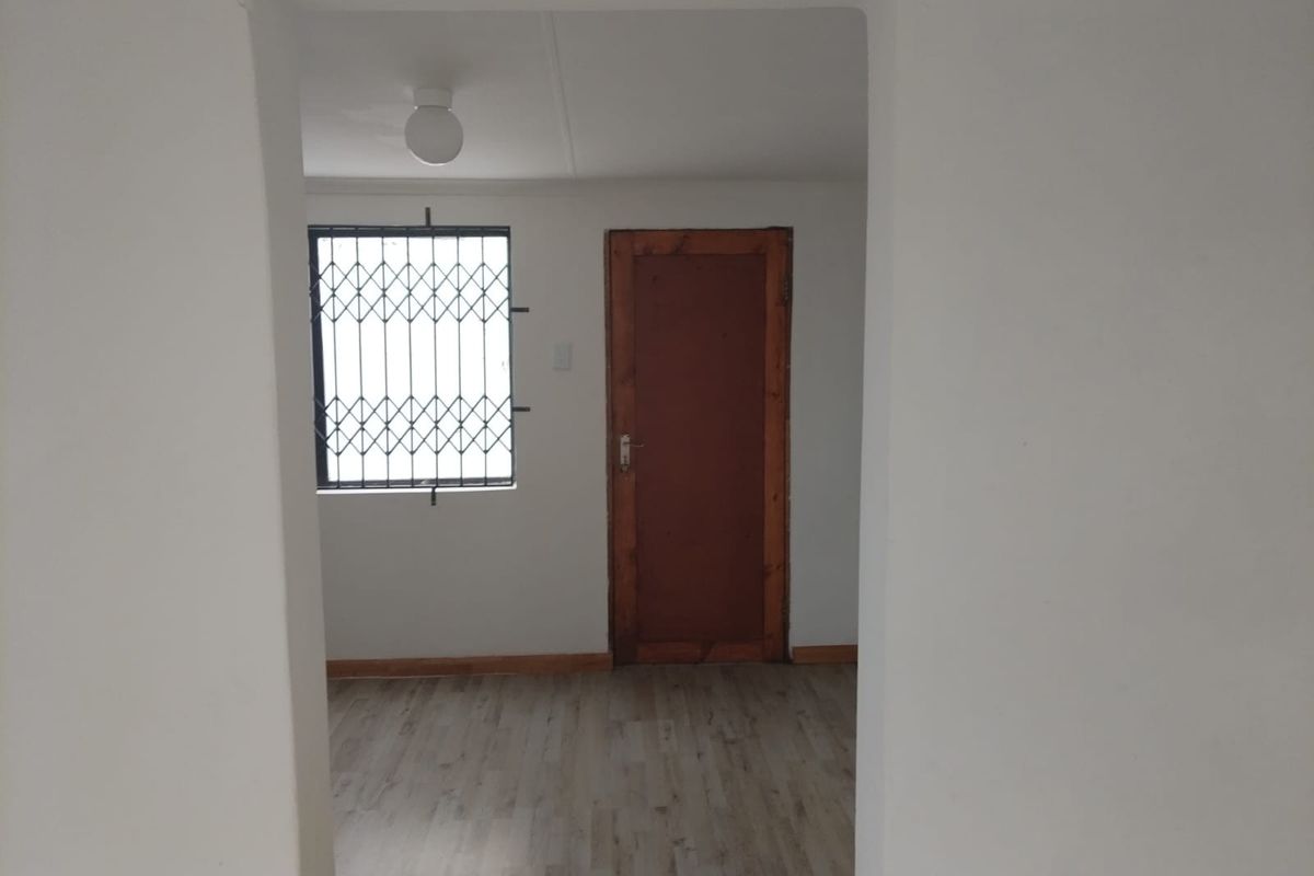 An empty bedroom featuring laminate flooring, a security gate on the window, and a timber door.