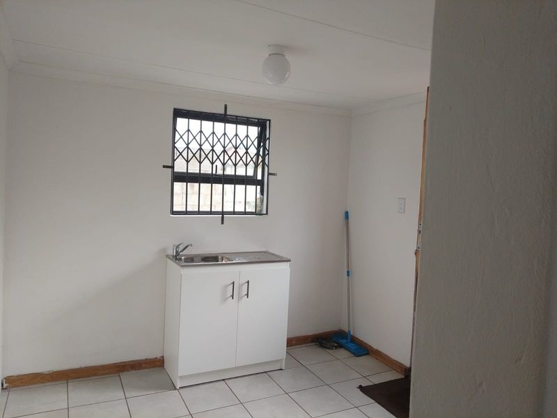 A compact kitchen area featuring a single stainless steel sink unit, tiled flooring, and a window fitted with a security gate.