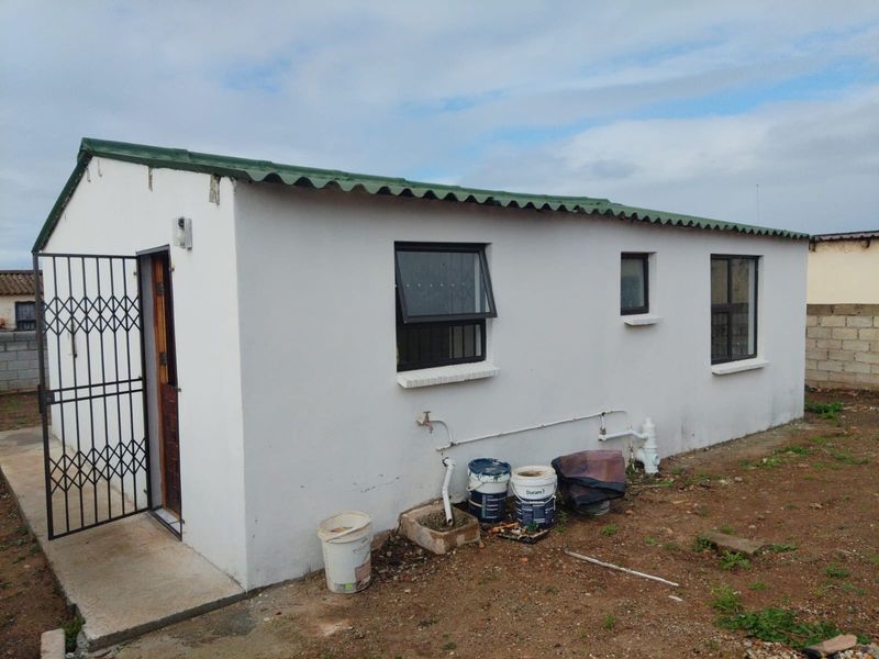 Rear view of a simple detached structure featuring a corrugated metal roof, security gate, and basic aluminium windows with exposed exterior plumbing.