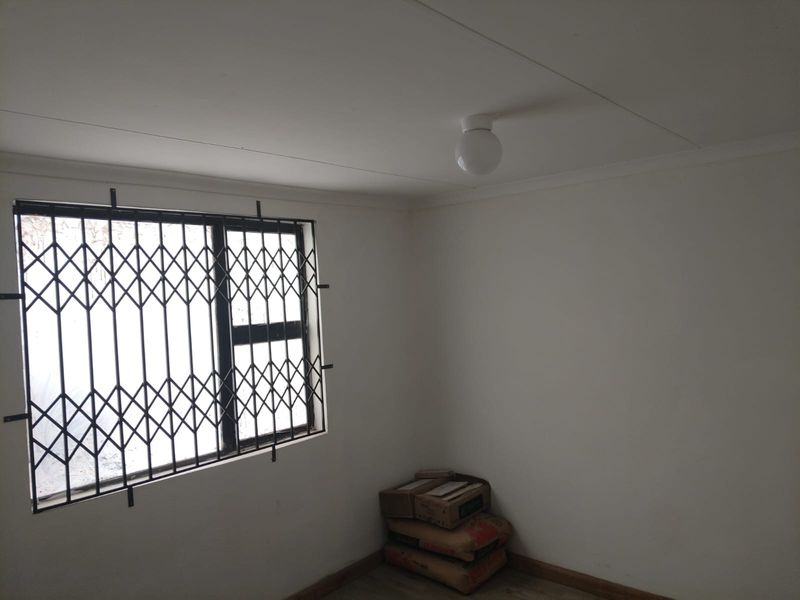 A simple, vacant bedroom featuring a window with a security gate and a basic ceiling light fixture.