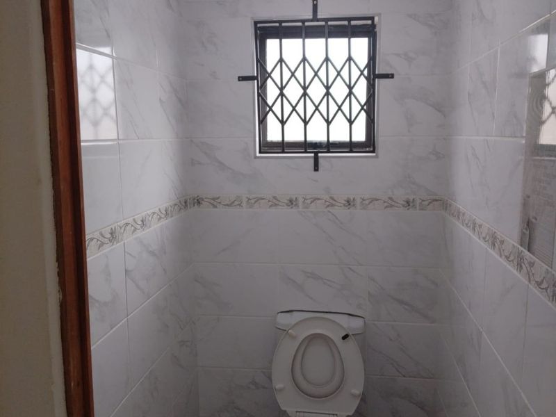 A compact, well-maintained guest bathroom featuring floor-to-ceiling marble-look wall tiles, a pedestal basin, and a secure window.