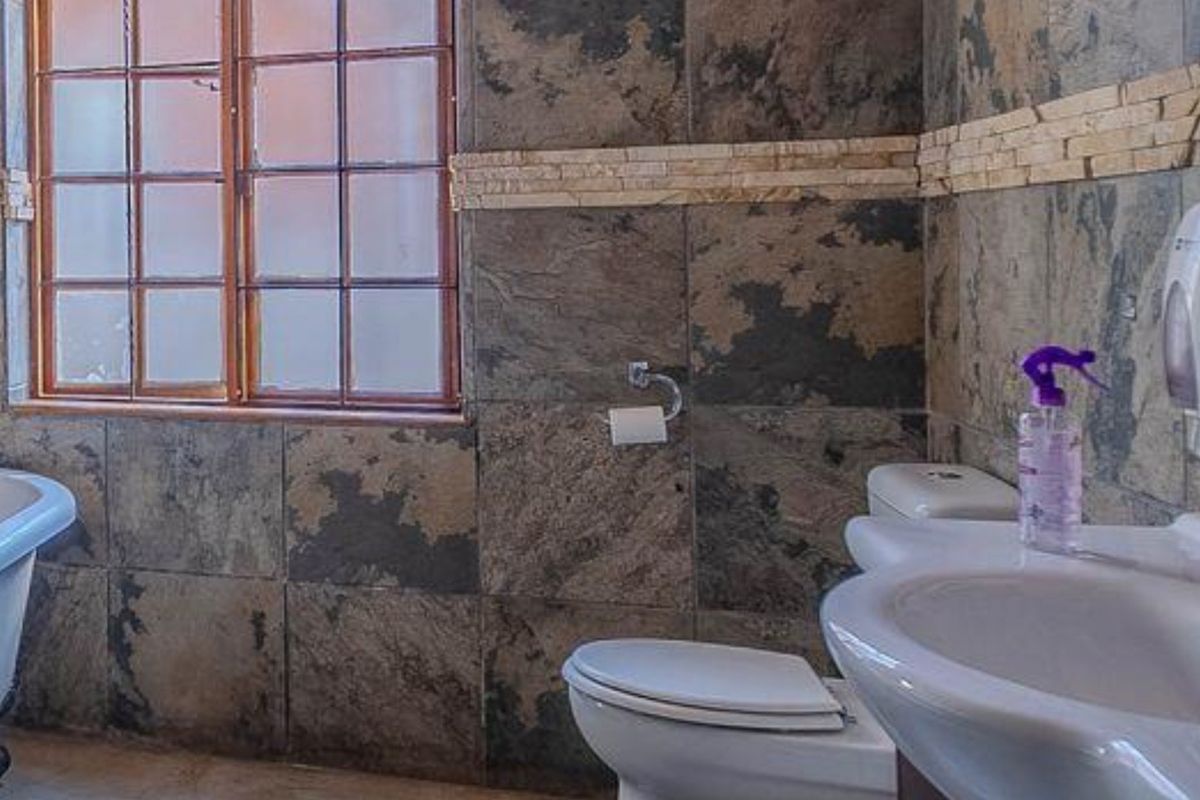 A bathroom featuring slate wall tiles with stone accents, a freestanding bathtub, a pedestal basin, and a timber-framed window.