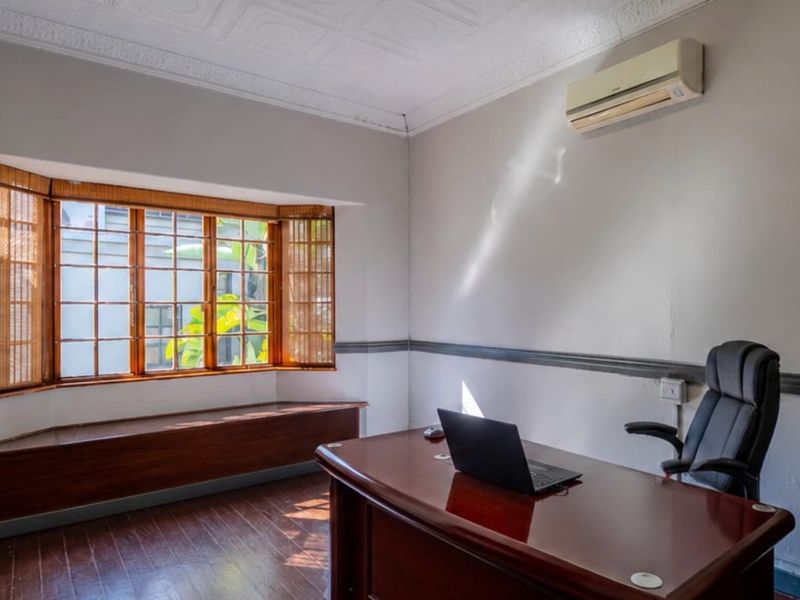 A home office featuring timber flooring, a bay window with wooden frames, decorative ceiling tiles, and a wall-mounted air conditioning unit.