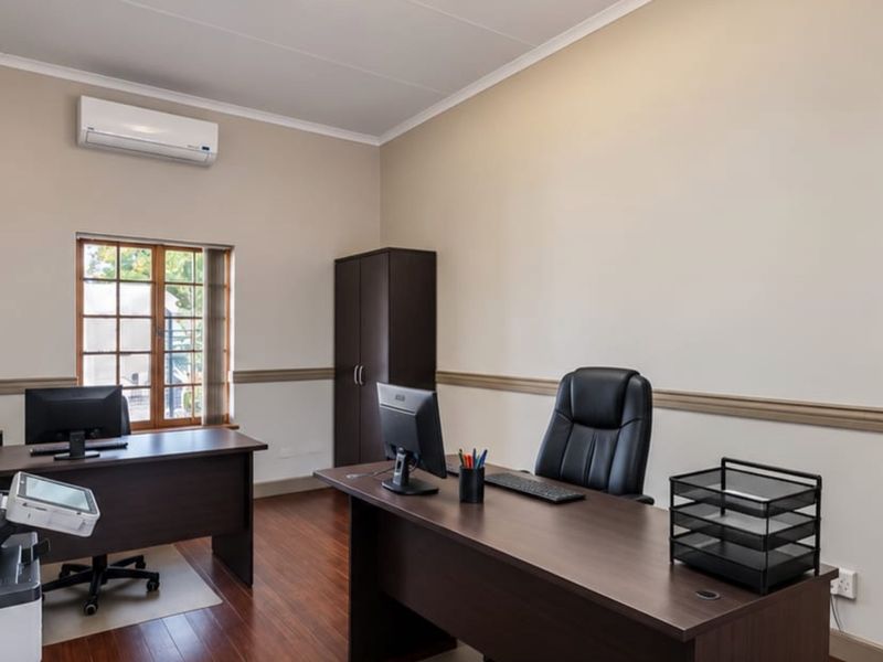 A well-maintained home office featuring timber-look flooring, a split-system air conditioner, and classic chair rail detailing.