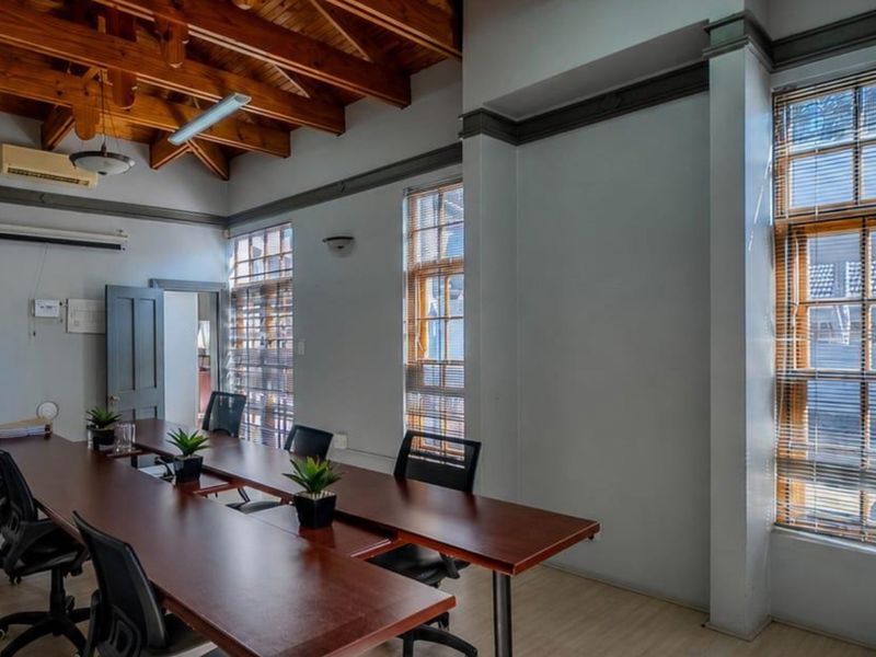 A professional office space featuring high exposed timber beam ceilings, large windows with venetian blinds, and neutral wall finishes.