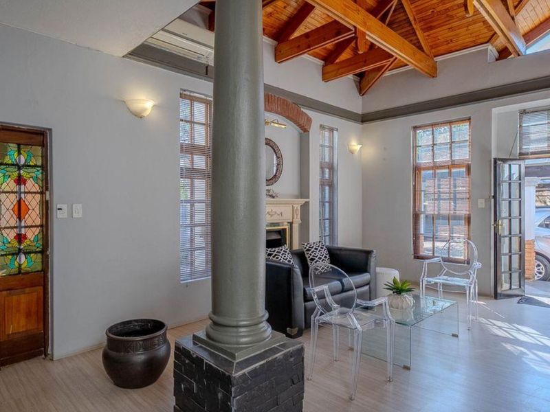 Spacious living room featuring exposed timber ceiling beams, a central brick column, a fireplace, and elegant stained glass entrance doors.
