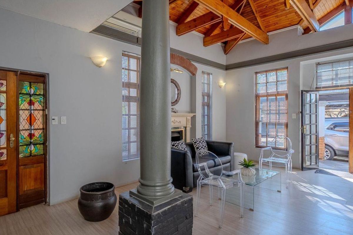 Spacious living room featuring exposed timber ceiling beams, a central brick column, a fireplace, and elegant stained glass entrance doors.