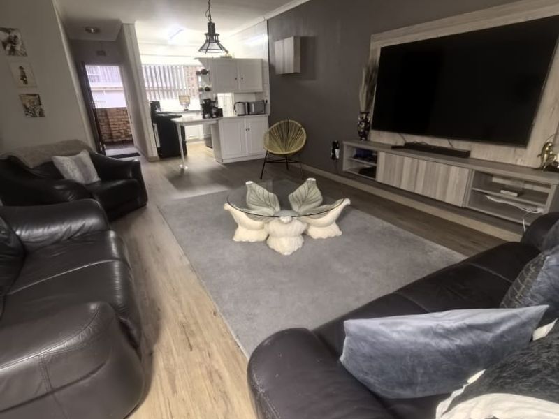 Open-plan living area featuring laminate flooring, a built-in media console, and a connected kitchen space with white cabinetry.