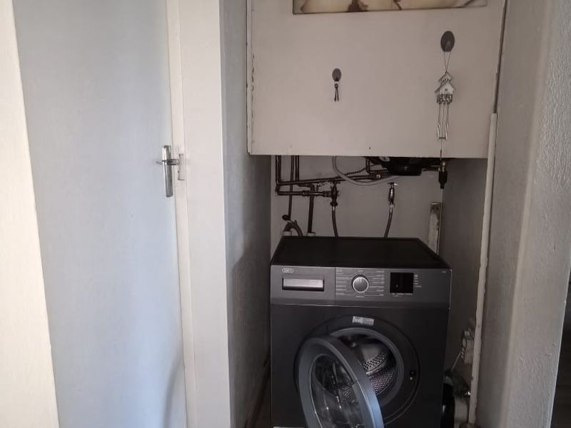 A compact laundry nook featuring exposed plumbing connections and laminate flooring, requiring finishing to improve the aesthetic and functionality of the space.