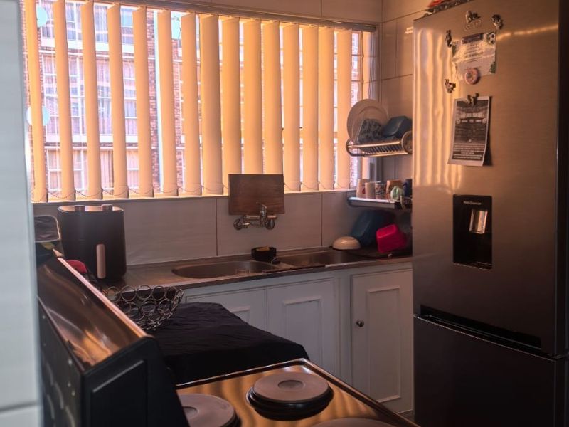 A functional kitchen featuring tiled walls, built-in cabinetry, a stainless steel sink, and an electric stove, illuminated by natural light through vertical blinds.