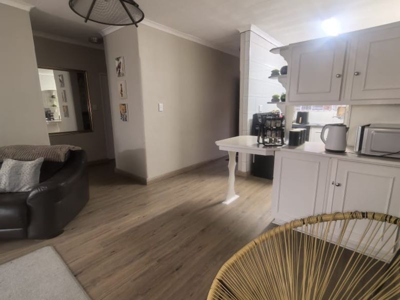 Open plan living area featuring light wood-look laminate flooring, neutral wall tones, and a functional kitchen space with built-in cabinetry.