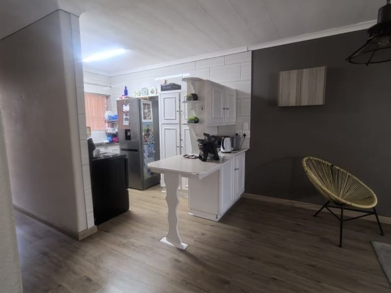 Open plan kitchen and living area featuring laminate flooring, white cabinetry, and a breakfast bar, offering a functional layout for modern apartment living.