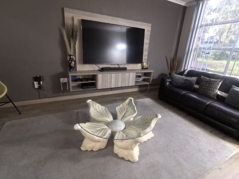 A well-maintained living room featuring a modern built-in media console, laminate flooring, and large windows with vertical blinds.