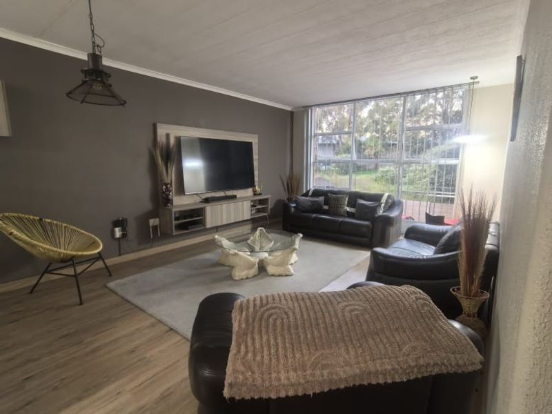 Spacious living room featuring modern laminate flooring, a built-in media console, and large windows that provide ample natural light.