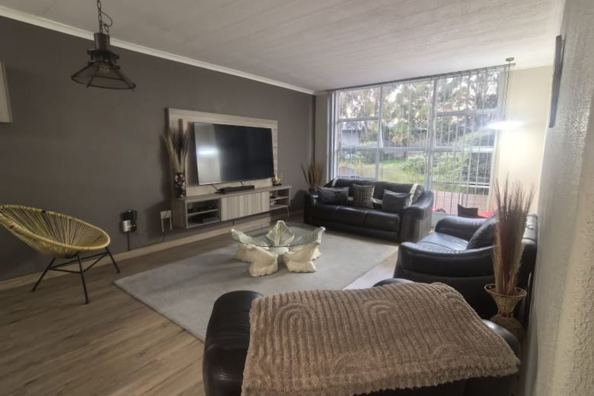 Spacious living room featuring modern laminate flooring, a built-in media console, and large windows that provide ample natural light.