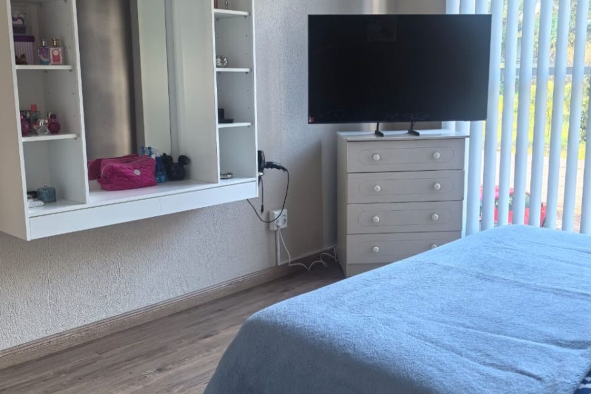 A bedroom featuring laminate flooring, vertical blinds, and a built-in wall-mounted shelving unit with an integrated mirror.