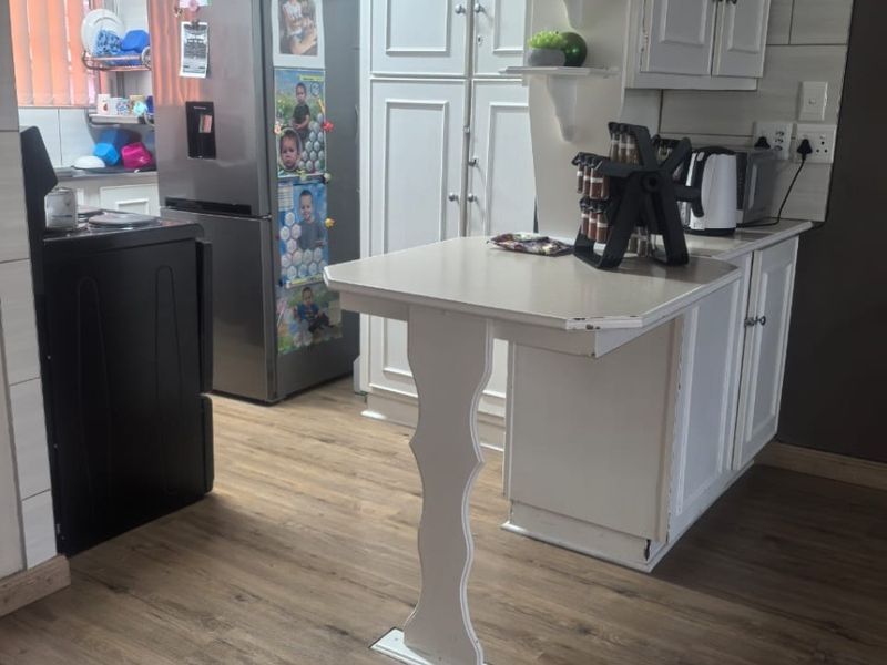 A functional kitchen featuring white cabinetry, a breakfast bar, wood-look laminate flooring, and a tiled backsplash.