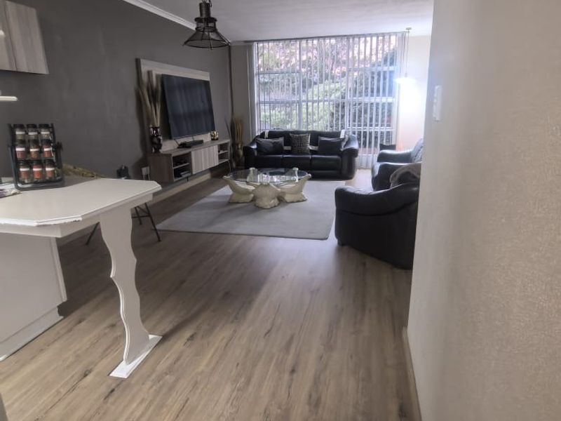 A spacious living room featuring modern laminate flooring, a built-in media console, and large windows with vertical blinds allowing for natural light.