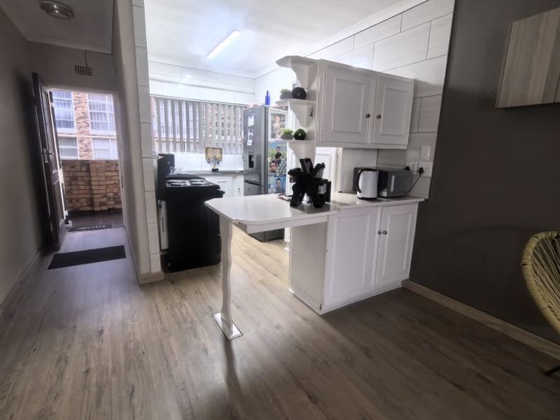 A functional kitchen area featuring built-in white cabinetry, a breakfast bar, and modern laminate flooring, with direct access to an outdoor balcony.