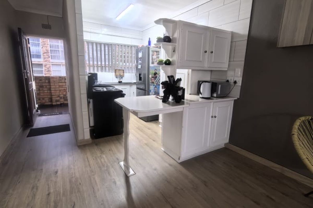 A functional kitchen area featuring built-in white cabinetry, a breakfast bar, and modern laminate flooring, with direct access to an outdoor balcony.