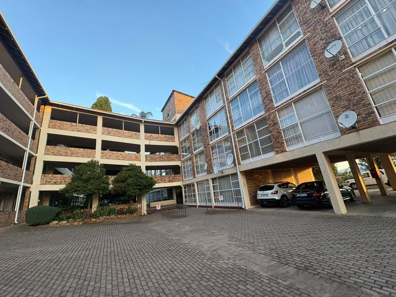 Exterior view of a multi-story face brick apartment complex featuring a paved courtyard and covered parking areas.