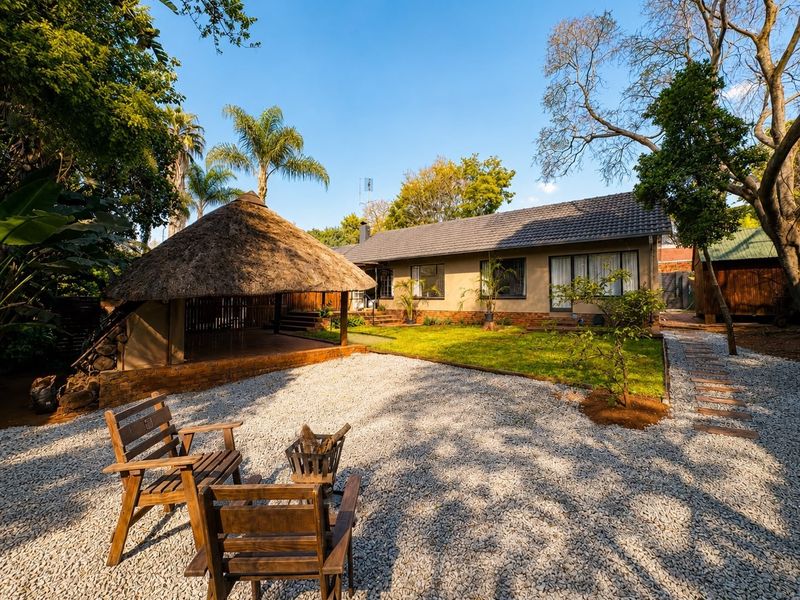 A well-maintained rear garden featuring a traditional thatched lapa, gravel landscaping, and a neat lawn area adjacent to the main house structure.