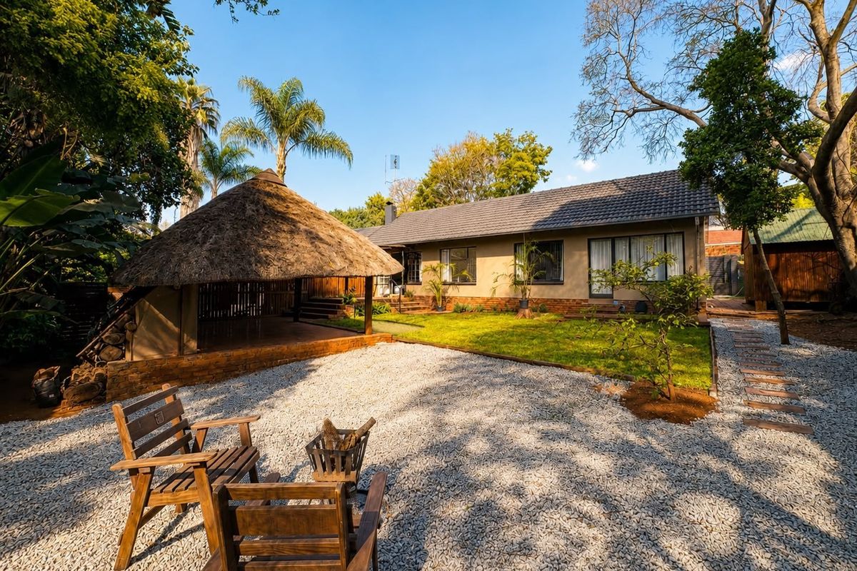 A well-maintained rear garden featuring a traditional thatched lapa, gravel landscaping, and a neat lawn area adjacent to the main house structure.