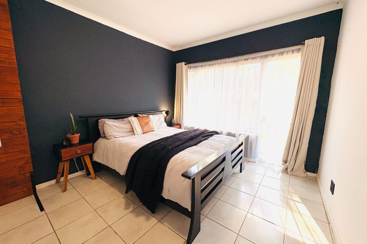 A well-maintained bedroom featuring tiled flooring, a dark accent wall, and a large sliding glass door providing natural light.