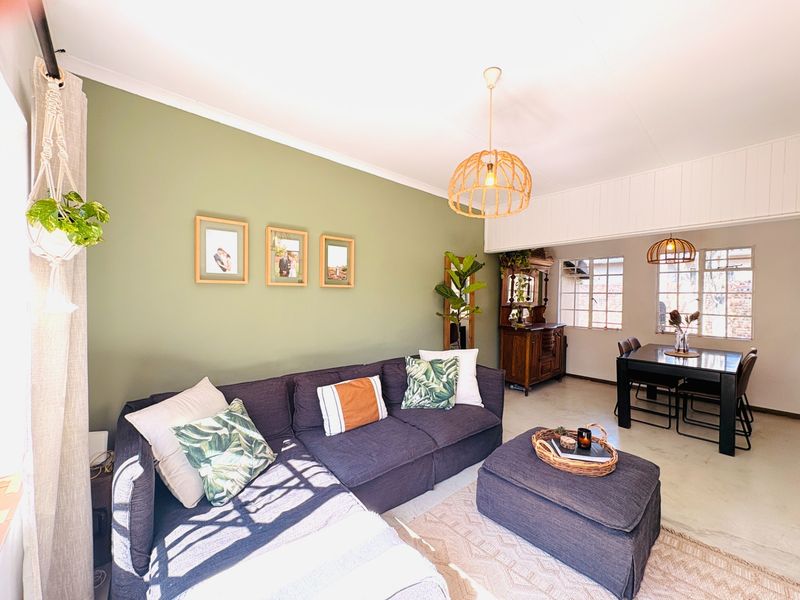 An open-plan living and dining area featuring concrete flooring, steel-framed windows, and decorative pendant lighting.