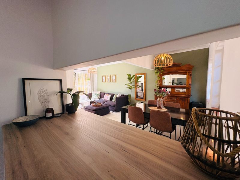 An open-plan living and dining area featuring a timber breakfast bar, neutral walls, and an accent wall, creating a warm and inviting atmosphere.