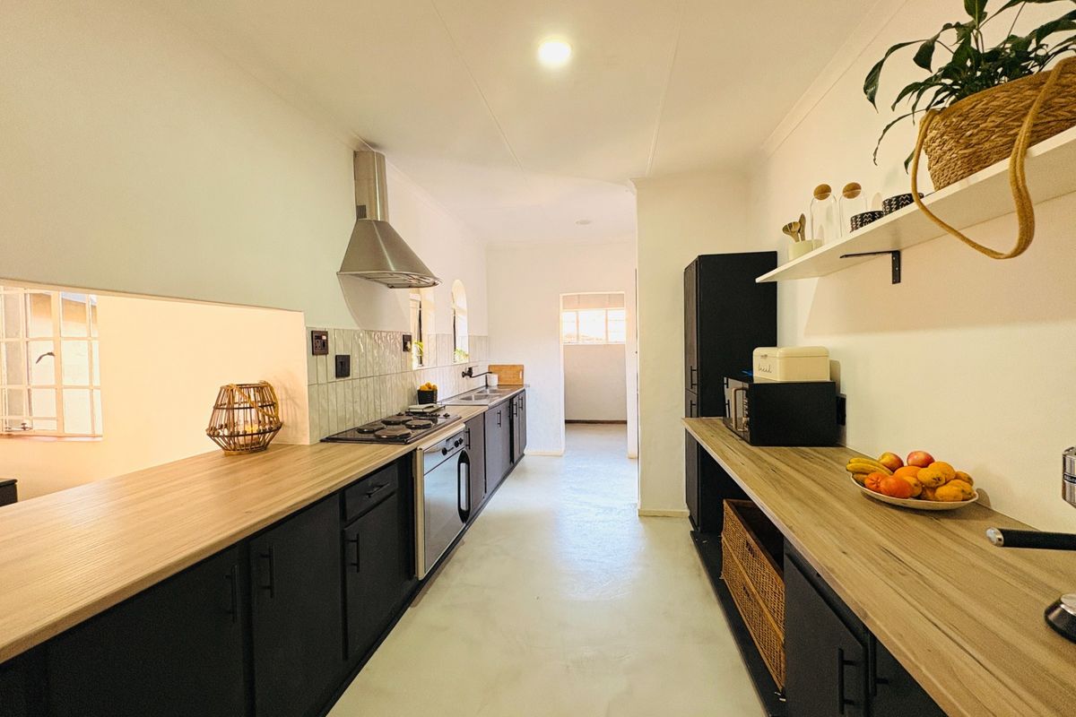 Modern galley-style kitchen featuring dark cabinetry, light wood-look countertops, stainless steel appliances, and a clean tiled backsplash.