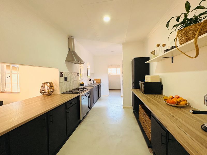 Modern galley-style kitchen featuring dark cabinetry, light wood-look countertops, stainless steel appliances, and a clean tiled backsplash.