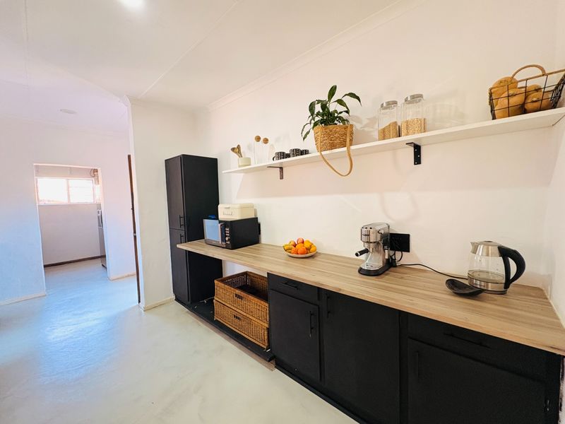 A modern kitchen area featuring black base cabinetry, wood-look countertops, and open wall shelving, providing a clean and functional prep space.