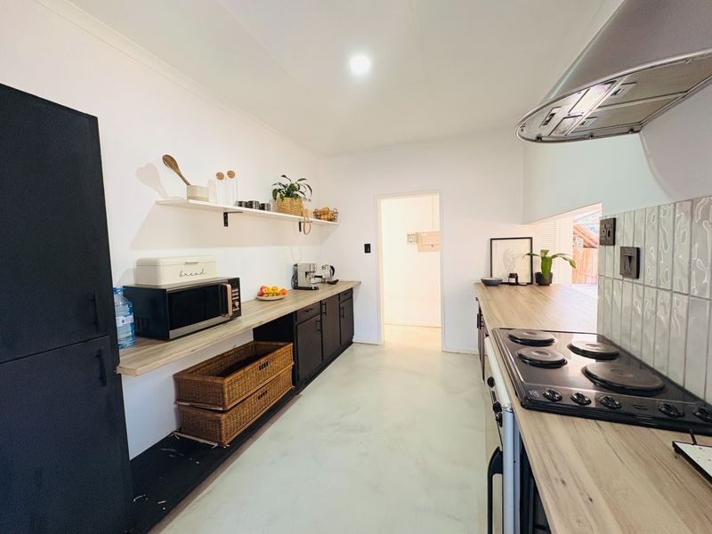Modern kitchen featuring dark cabinetry, light wood-look countertops, electric hob with extractor fan, and a clean tiled backsplash.