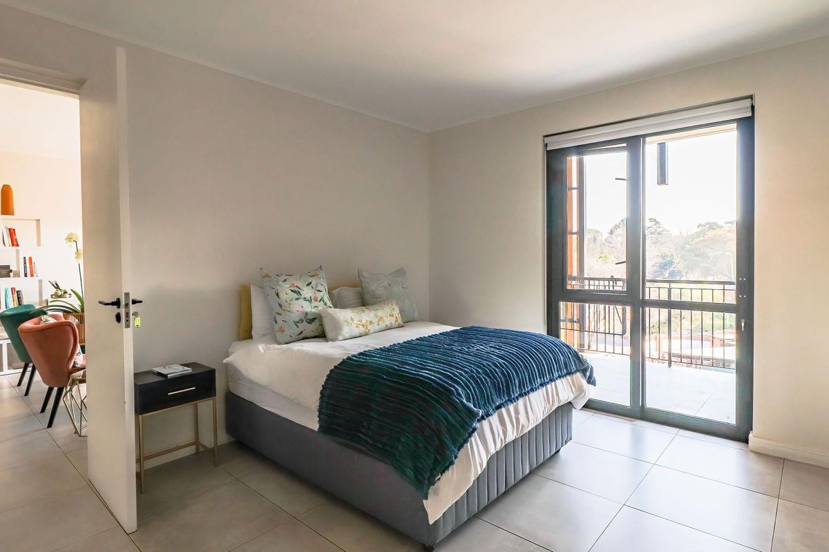A bright bedroom featuring neutral walls, large format floor tiles, and a sliding glass door providing access to a private balcony.