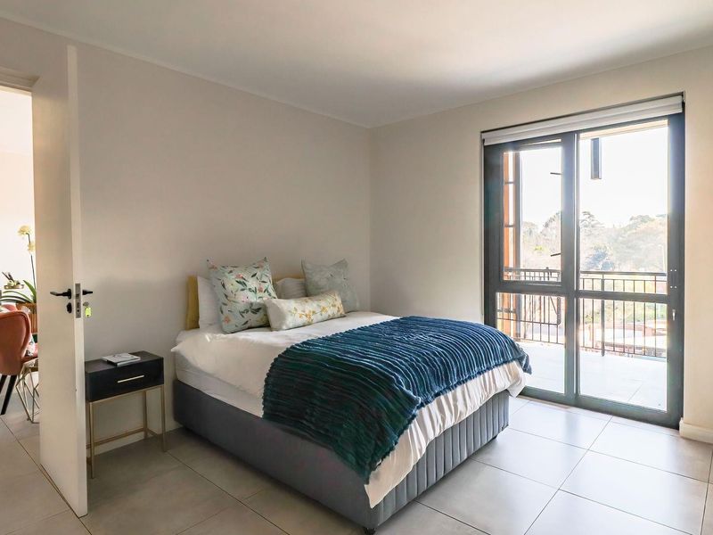A bright bedroom featuring neutral walls, large format floor tiles, and a sliding glass door providing access to a private balcony.
