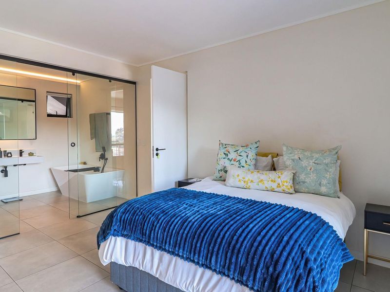 Modern bedroom featuring an open-concept glass-enclosed ensuite bathroom with a sleek freestanding bathtub and contemporary wall-mounted vanity.
