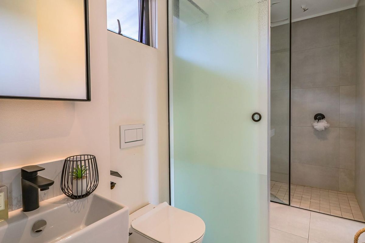 Modern bathroom featuring a walk-in shower with a frosted glass screen, wall-mounted toilet, and a sleek basin with matte black fixtures.