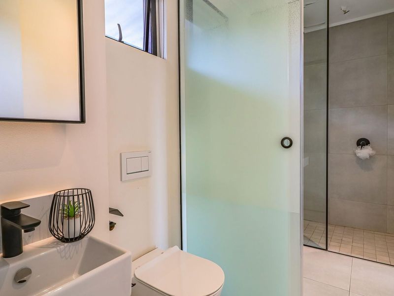 Modern bathroom featuring a walk-in shower with a frosted glass screen, wall-mounted toilet, and a sleek basin with matte black fixtures.